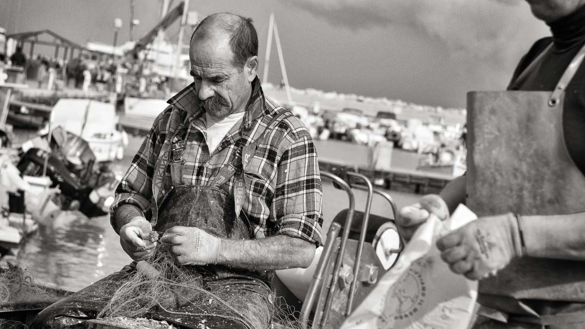 Un pescatore sbroglia la rete seduto in barca: qui vedi cosa sta facendo. Il progetto racconta chi è.