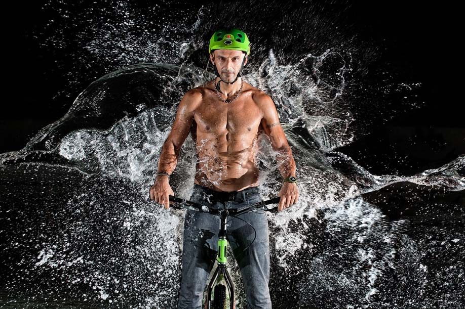 Un uomo in sella a una mountain bike, di notte, investito da uno schizzo d'acqua: le gocce restano ferme a mezz'aria, staccate una dall'altra.