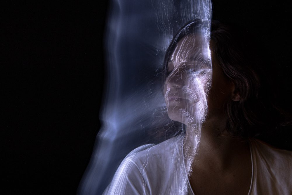 Una donna con gli occhi chiusi e un velo di luce che le passa davanti al viso come una tenda.