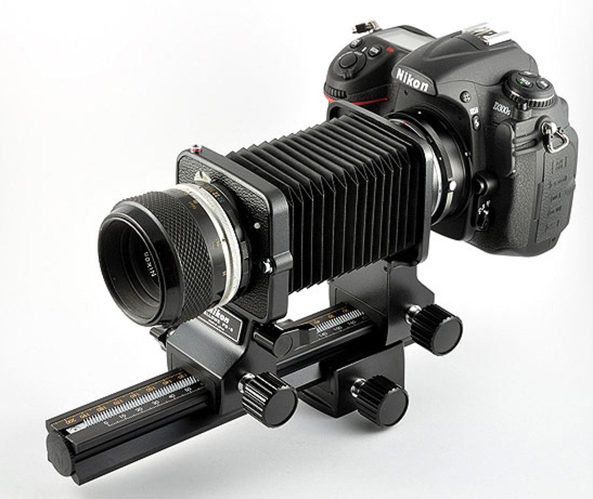 Una fotocamera con un soffietto montato fra il corpo e l'obiettivo. Sotto la fotocamera c'è una slitta micrometrica.